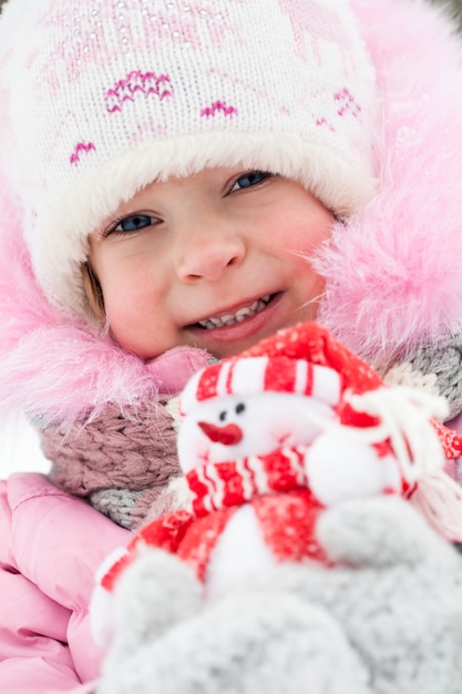 Ritratto del primo piano del bambino felice che tiene la decorazione di Natale nell'inverno