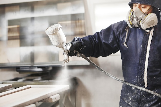 Ritratto del primo piano del lavoratore che utilizza la pistola a spruzzo e la pittura del legno