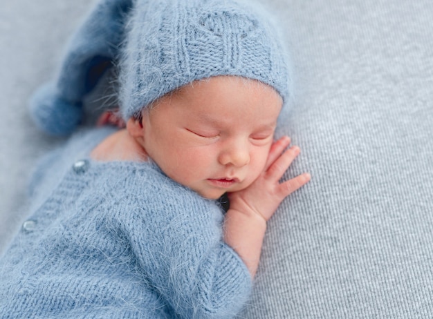 Ritratto del primo piano del neonato che indossa vestito blu chiaro lavorato a maglia e cappello che dorme