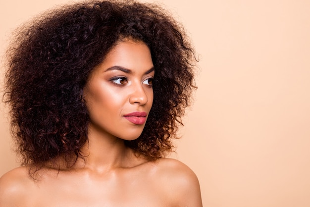 Ritratto del primo piano dell'affascinante ragazza dai capelli ondulati isolata sopra la parete pastello beige