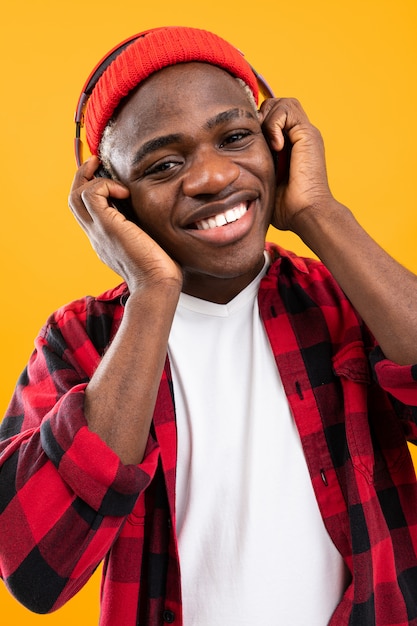 Ritratto del primo piano dell'uomo africano bello in camicia a quadretti rossa che ascolta la musica sulle cuffie