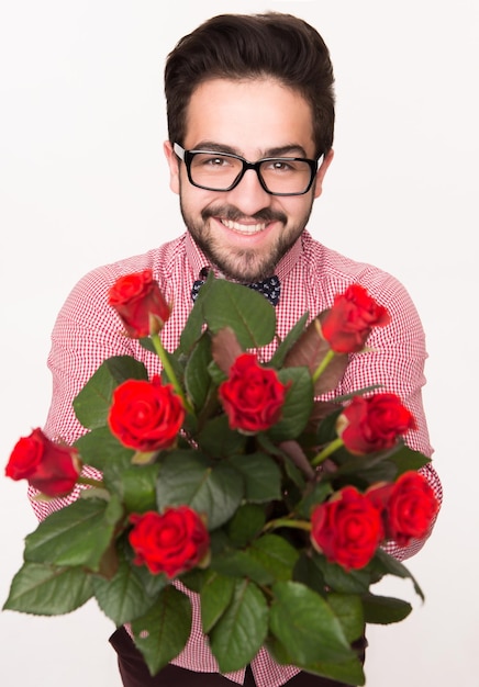 Ritratto del primo piano dell'uomo barbuto bello in vetri che tengono un mazzo di rose su bianco.