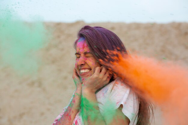 Ritratto del primo piano della donna castana espressiva che gioca con la pittura asciutta variopinta Holi al deserto