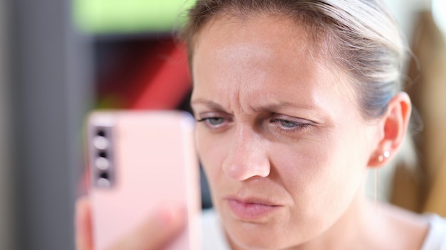 Ritratto del primo piano della donna che guarda il display dello smartphone da vicino con problemi agli occhi