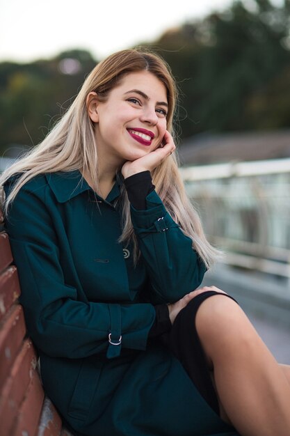 Ritratto del primo piano della ragazza bionda allegra che indossa cappotto verde. Spazio per il testo