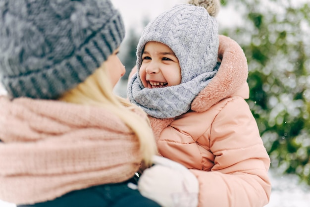 Ritratto del primo piano della vista posteriore della bambina felice che sorride e che gioca insieme a sua madre nel parco il giorno della nevicata Bella donna e suo figlio che camminano nel giorno d'inverno Atmosfera natalizia Infanzia