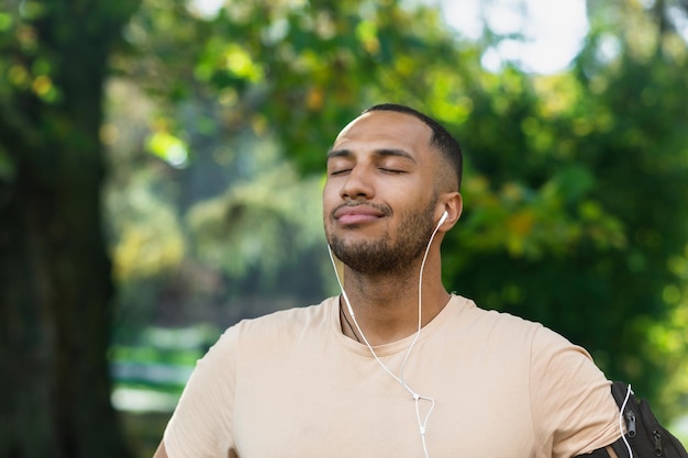 Ritratto del primo piano dello sportivo nel parco uomo ispanico che fa jogging nel parco con gli occhi chiusi respirando fresco