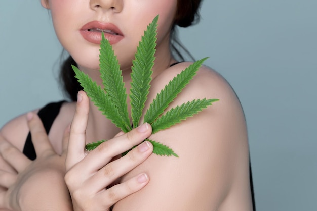 Ritratto del primo piano di affascinante ragazza grassoccia con la pelle fresca che tiene la foglia di cannabis