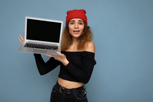 Ritratto del primo piano di bella donna bionda scura che tiene computer portatile che esamina macchina fotografica che mostra a