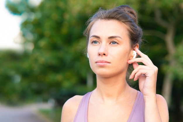 Ritratto del primo piano di bella giovane donna pensierosa che parla tramite le cuffie del bluetooth mentre a spor...