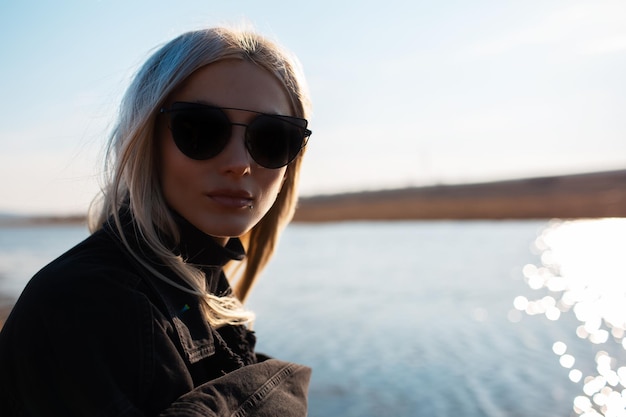 Ritratto del primo piano di bella ragazza bionda che indossa occhiali da sole vicino al fiume