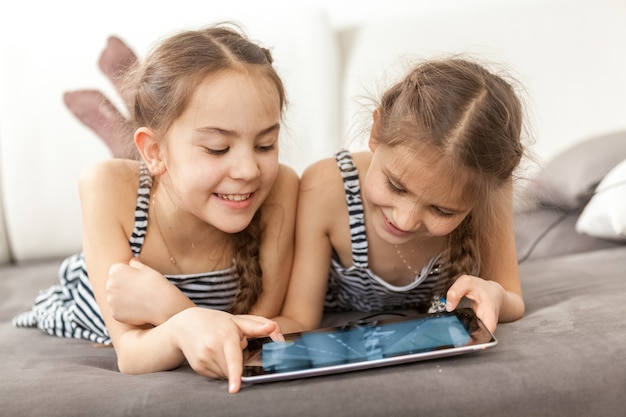 Ritratto del primo piano di due ragazze sorridenti sdraiate sul divano e usando il tablet