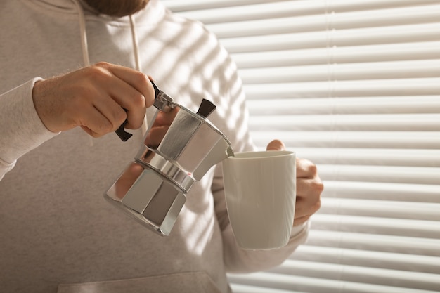 Ritratto del primo piano di giovane uomo alla moda hipster versando il caffè in ufficio il giorno d'estate. Mattina tonificante e umore positivo