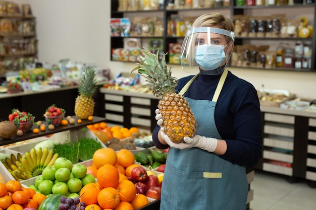 Ritratto del primo piano di un lavoratore femminile sorridente felice del negozio di alimentari che indossa una maschera protettiva