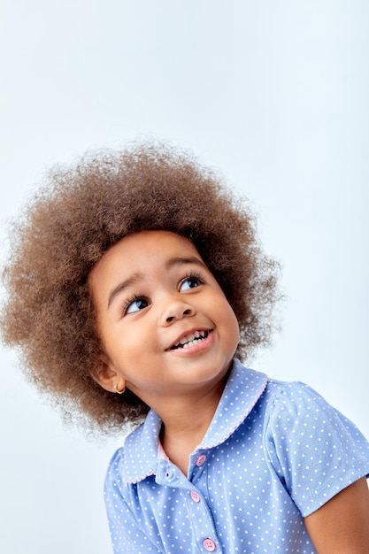 Ritratto del primo piano di una bambina africana sorpresa carina in maglietta blu che guarda qualcosa di interes...