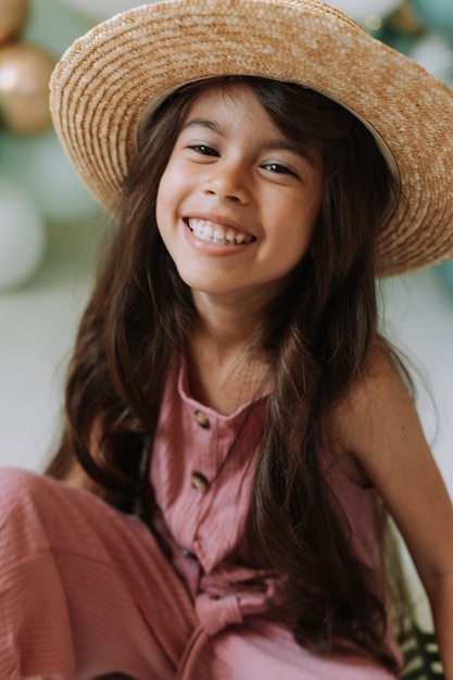 Ritratto del primo piano di una bella bambina sorridente con gli occhi marroni e capelli scuri in un cappello di paglia