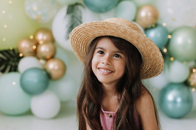 Ritratto del primo piano di una bella bambina sorridente con gli occhi marroni e capelli scuri in un cappello di paglia