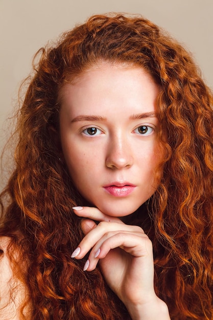 Ritratto del primo piano di una bella ragazza con lunghi capelli rossi ricci. Studio girato su sfondo beige