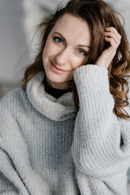 Ritratto del primo piano di una giovane donna abbastanza sorridente in maglione accogliente che guarda l'obbiettivo.