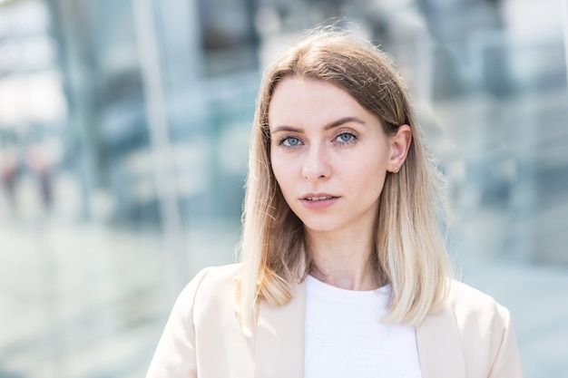 Ritratto del primo piano di una giovane donna felice in piedi all'aperto e sorridente su sfondo urbano sfocato che guarda l'obbiettivo. Donna bionda con gli occhi azzurri che ride con uno studente con bei denti bianchi Primo piano