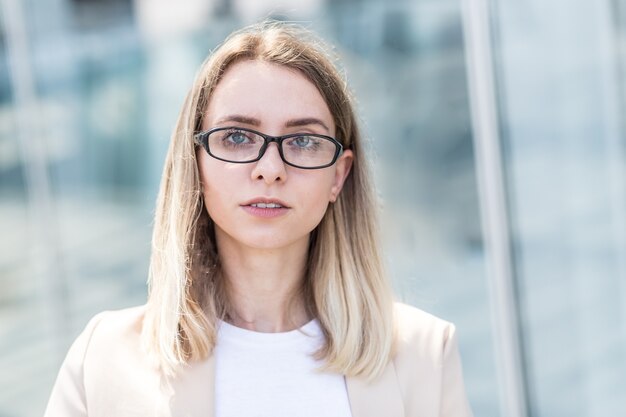 Ritratto del primo piano di una giovane donna felice in piedi all'aperto e sorridente su sfondo urbano sfocato che guarda l'obbiettivo. Donna bionda con gli occhi azzurri che ride con uno studente con bei denti bianchi Primo piano