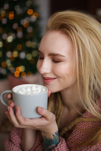 Ritratto del primo piano di una ragazza sorridente allegra con i dreadlocks con una tazza di cacao con marshmallow