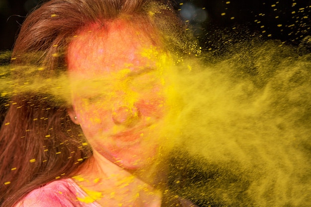 Ritratto del primo piano di una straordinaria donna bruna con vernice Holi che le soffia in faccia