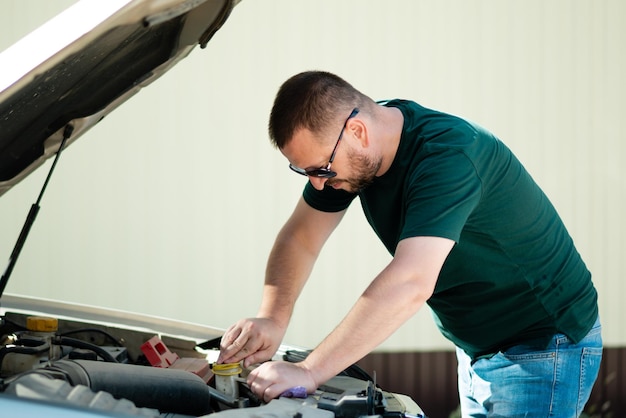 Ritratto del primo piano giovane che ha problemi con il suo cofano ad apertura automatica rotto che cerca di riparare il motore.