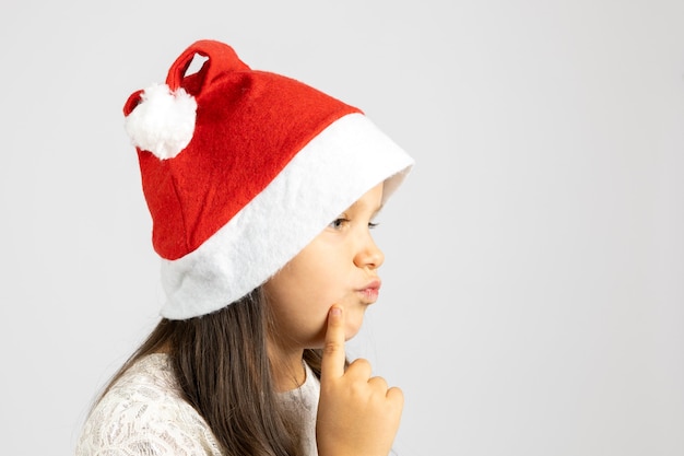 Ritratto del primo piano nel profilo della ragazza premurosa in cappello di babbo natale con il dito sul m...