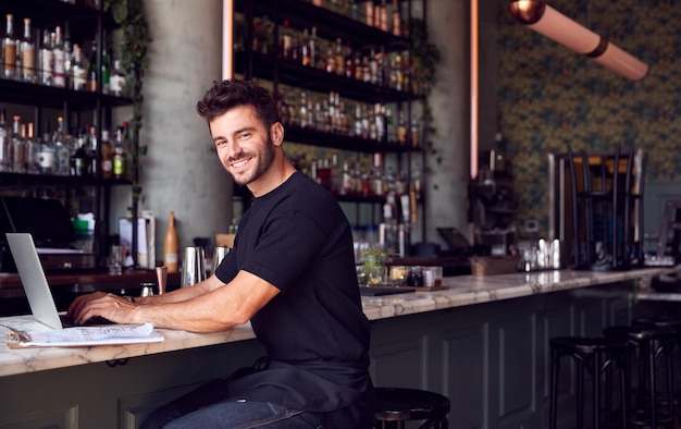 Ritratto del proprietario maschio del bar del ristorante che si siede al bancone che lavora al computer portatile