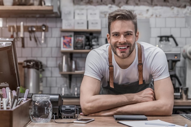 Ritratto del proprietario maschio sorridente della caffetteria che sta dietro il bancone