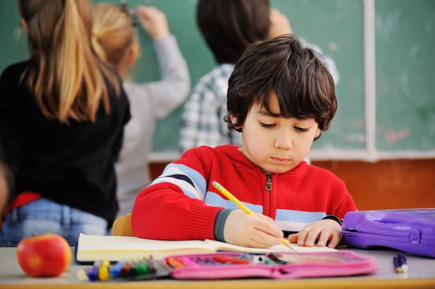 Ritratto del ragazzo adorabile che assorbe quaderno a scuola