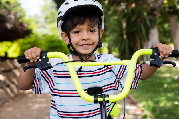 Ritratto del ragazzo sorridente che sta con la bicicletta in parco