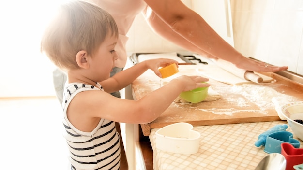 Ritratto del ragazzo sveglio del bambino di 3 anni che cucina i biscotti con la madre. Cucina e pasticceria in famiglia