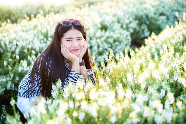 Ritratto del viaggiatore felice della giovane donna asiatica con il vestito bianco e nero del modello che gode nel campo di fiori in fiore bianco nel giardino della natura in vacanza di relax di Thailandtravel
