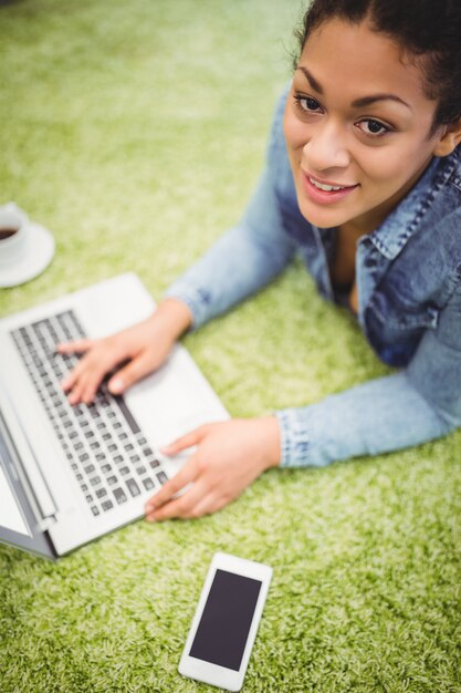 Ritratto dell'angolo alto della donna di affari che per mezzo del computer portatile sul tappeto