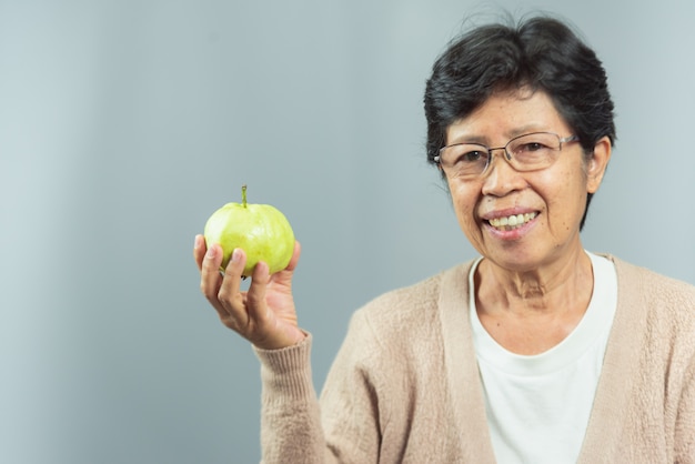Ritratto dell'anziana sorridente che tiene frutta verde su gray