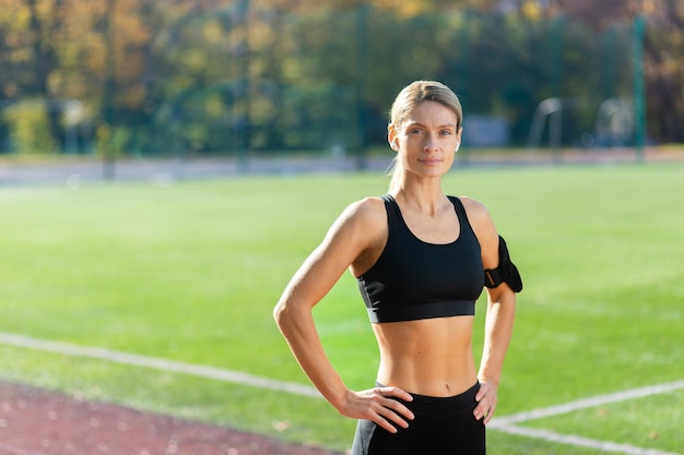 Ritratto dell'atleta femminile adulto maturo nello stadio atleta femminile che si tiene per mano sui fianchi sorridendo e