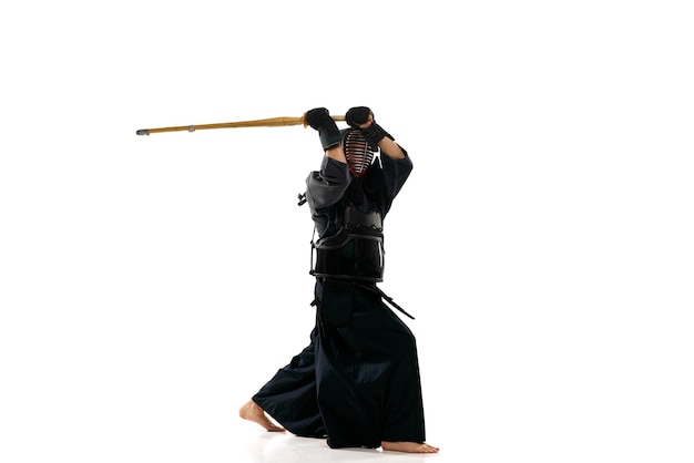 Ritratto dell'atleta professionista di kendo dell'uomo in formazione uniforme in posa con la spada shinai su sfondo bianco studio