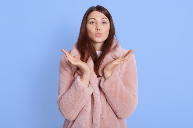 Ritratto dell'interno di giovane ragazza abbastanza europea che indossa un cappotto alla moda di pelliccia sintetica rosa pallido