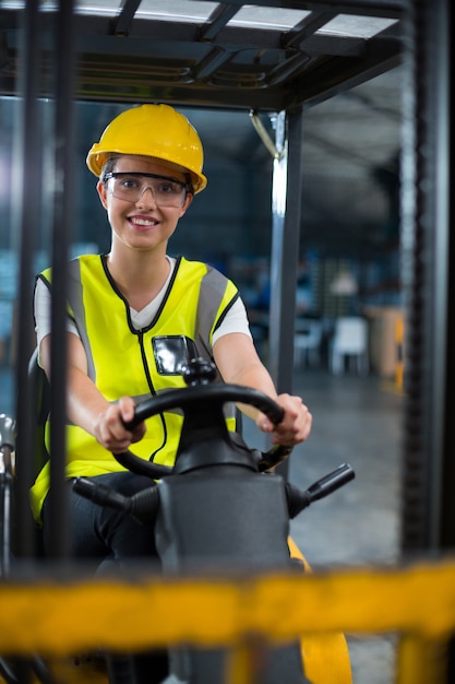 Ritratto dell'operaio femminile sorridente che guida carrello elevatore