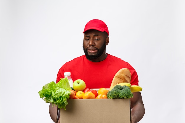 Ritratto dell'uomo afroamericano di consegna in camicia rossa. solleva scatole di generi alimentari pesanti