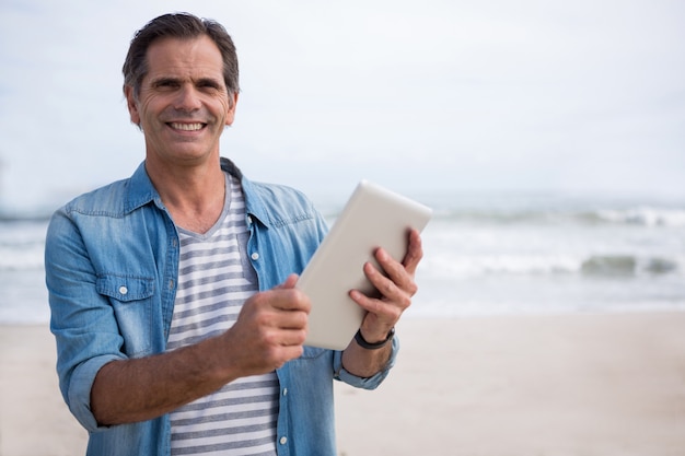 Ritratto dell'uomo che per mezzo della compressa digitale sulla spiaggia