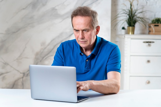 Ritratto dell'uomo concentrato maturo anziano anziano bello che lavora usando la sua digitazione del computer portatile