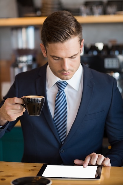 Ritratto dell'uomo d'affari che utilizza compressa digitale nel caffè