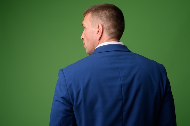 Ritratto dell'uomo d'affari macho maturo che porta vestito blu contro la chiave di crominanza con la parete verde