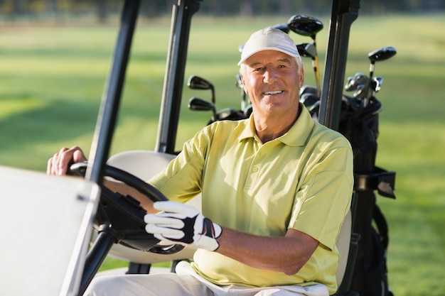 Ritratto dell'uomo maturo sorridente che guida il buggy di golf