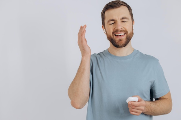 Ritratto dell'uomo moderno millenario con la barba che tiene gli auricolari wireless su sfondo bianco con spazio per la copia