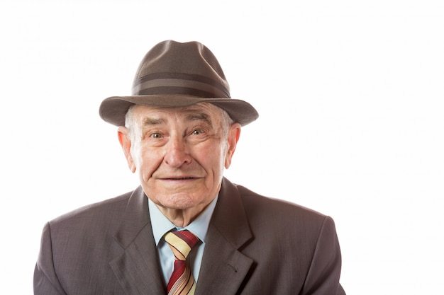 Ritratto dell'uomo senior di 90 anni in retro cappello che esamina macchina fotografica isolata su bianco