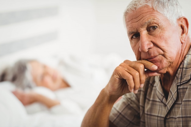 Ritratto dell'uomo senior preoccupato che si siede sul letto in camera da letto